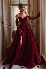 Woman in a burgundy evening gown with long gloves standing in an elegant interior setting.