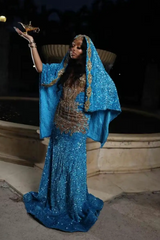 Woman in a blue and gold dress holding a small object against a dark background